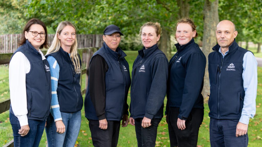 A group of Shadwell employees stand in a green setting smiling to camera